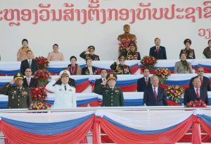 Presidents of the Lao PDR present and former standing to attention as military leaders salute.