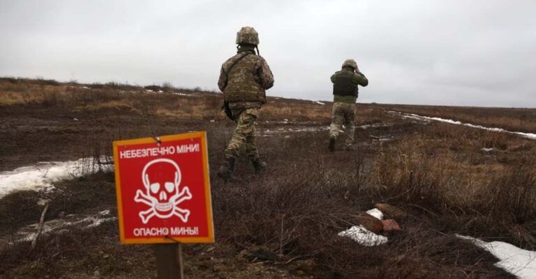 Ukrainian military servicemen walk past a sign which reads 'Caution mines' on the frontline in Donetsk region (Jan 2022, VOA).