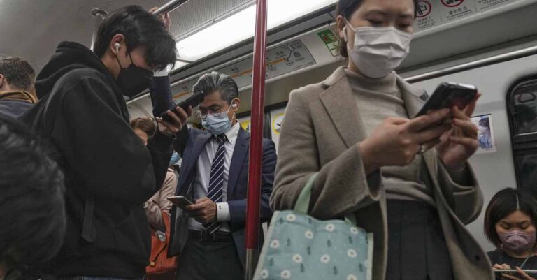 Commuters wearing face masks browse their smartphones as they ride on a subway train in Hong Kong on Feb. 7, 2023. Hong Kong will lift its mask mandate Wednesday, March 1, 2023, ending the city’s last major restriction imposed during the COVID-19 pandemic. (AP Photo/Andy Wong, File)