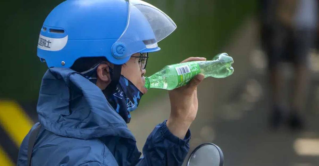 A delivery driver takes a drink as he waits at a traffic light on an unseasonably hot day in Beijing, Saturday, June 24, 2023. Authorities continued a rare red alert for high temperatures in parts of China's capital on Saturday, the highest level of warning, as highs were once again expected to climb to around 40 degrees Celsius (104 degrees Farenheit). (AP Photo/Mark Schiefelbein)