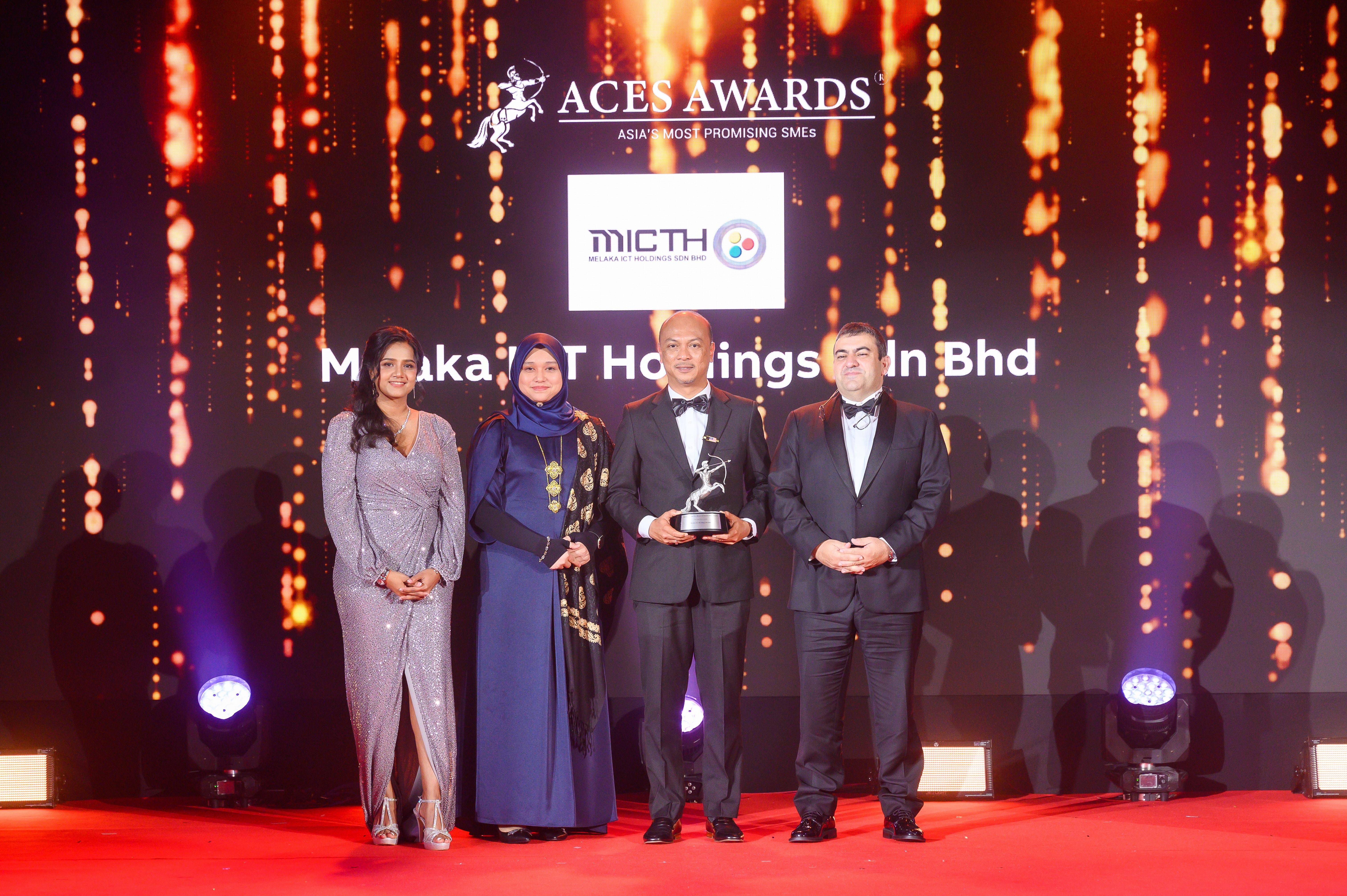 Dr. Nazdiana Ab Wahab, Chief Executive Officer of Melaka ICT Holdings Sdn Bhd (left center), and YB Datuk Fairul Nizam bin Roslan, Deputy Chairman of the Board of Directors (right center), proudly receive the Asia's Most Promising SMEs award on stage at the ACES Awards 2024. The award is presented by Dr. Shanggari Balakrishnan, President of the ACES Awards (far left), and Mr. Luis Bueno Nieto, Advisor to the ACES Council (far right), in recognition of the Melaka ICT Holdings Sdn Bhd's exceptional growth and promising future in the industry.