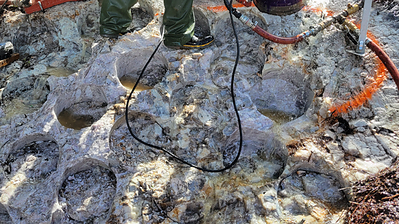 Figure 2: (TOP) Cored drill hole (~30 cm diameter) in pollucite pegmatite outcrop; (BOTTOM) Grid of cored drill holes (~30 cm diameter) in pollucite pegmatite outcrop (see Table 1). Segments between holes are jackhammered out and added to sample composite. Figure 2: (TOP) Cored drill hole (~30 cm diameter) in pollucite pegmatite outcrop; (BOTTOM) Grid of cored drill holes (~30 cm diameter) in pollucite pegmatite outcrop (see Table 1). Segments between holes are jackhammered out and added to sample composite.